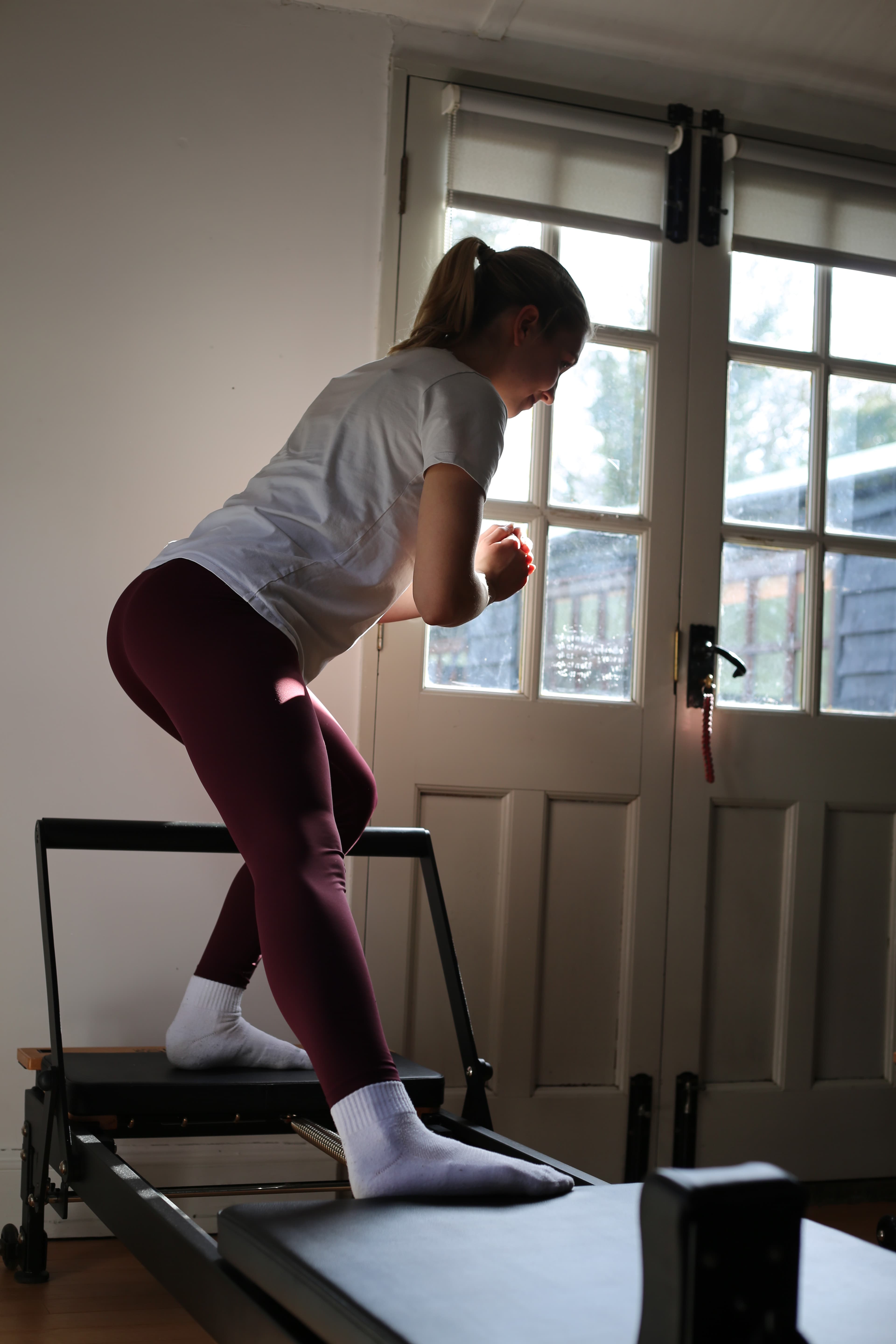 Member standing hinged on the reformer facing the studio's French doors
