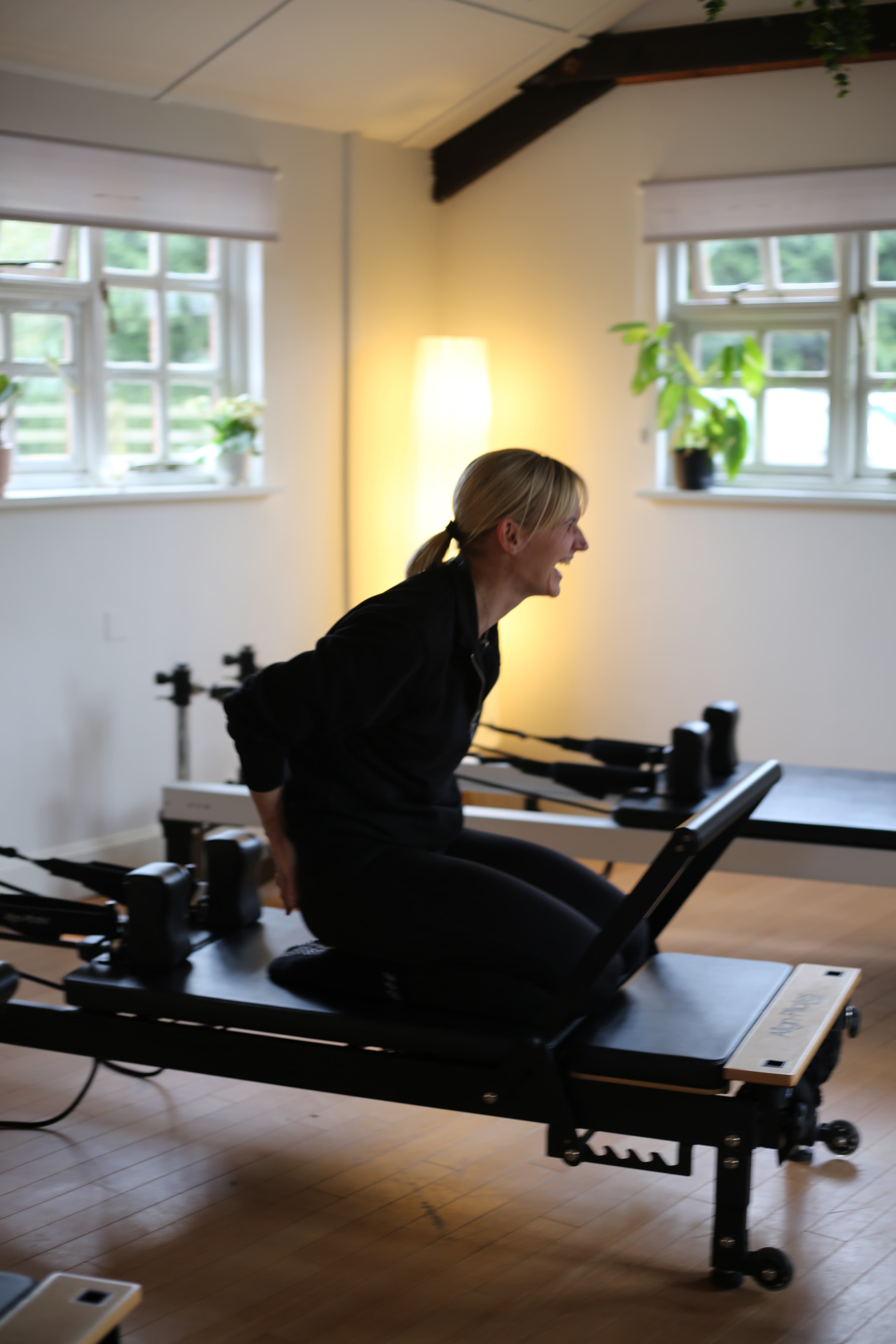 Sue Hoadley kneeling on a reformer in the studio, laughing